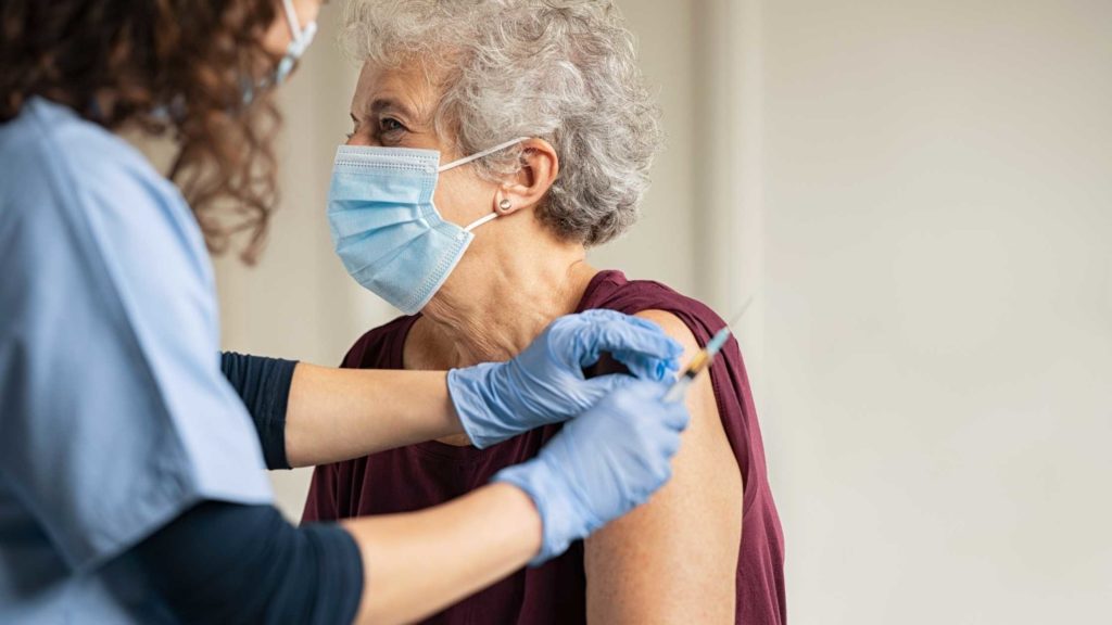 Se protéger contre la Covid-19 grâce à la vaccination illustré par une personne âgée se faisant vacciner dans un cabinet médicale.